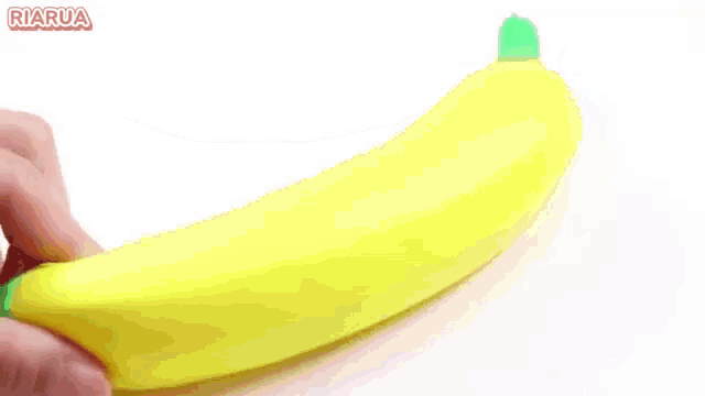 a person is holding a yellow banana with their hands on a white surface .