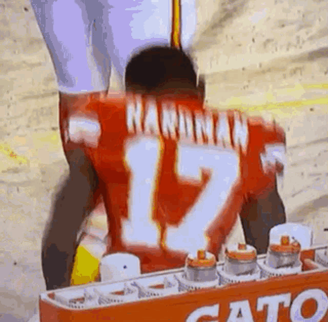 a football player wearing a red jersey with the number 12 on it is standing in front of a gatorade cooler .