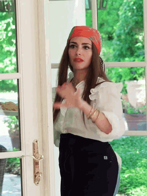 a woman wearing a head scarf and a white shirt is standing in front of a door