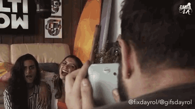 a man is taking a picture of two women on a couch with his cell phone .