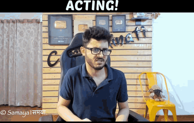 a man wearing glasses is sitting in front of a wall that says " acting " on it