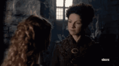 two women are standing next to each other in a dark room and one of them is holding another woman 's hand .