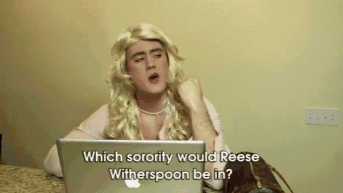a man in a wig is sitting in front of an apple laptop and asking which sorority would reese witherspoon