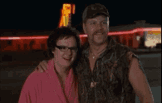 a man and a woman posing for a picture in front of a neon sign
