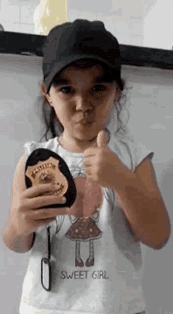 a little girl is wearing a hat and holding a police badge .