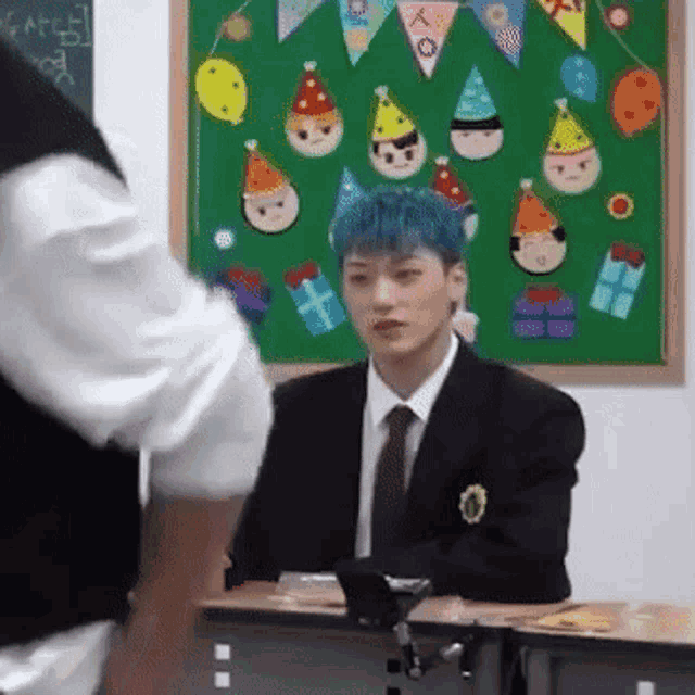 a man in a suit and tie is sitting at a desk in front of a classroom .