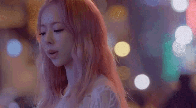 a woman with long pink hair is standing in front of a blurry background .