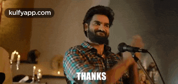 a man with a beard is standing in front of a microphone and saying `` thanks '' .