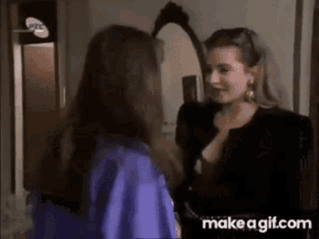 two women are standing next to each other in front of a mirror and talking .