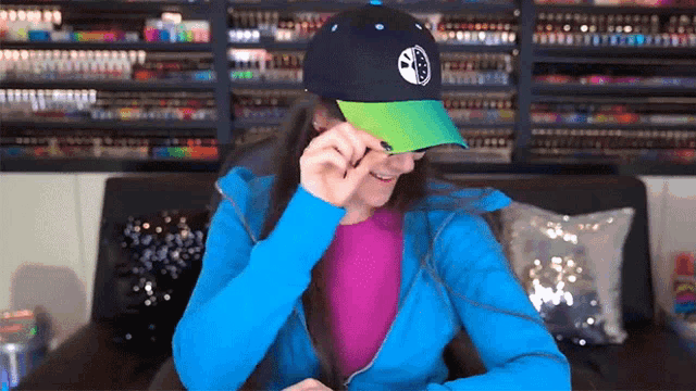 a woman wearing a blue jacket and a black hat with a green brim is smiling