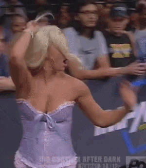 a woman in a purple corset is dancing in front of a crowd that is watching a wrestling match