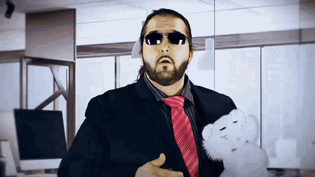 a man wearing sunglasses and a suit holds a stuffed animal