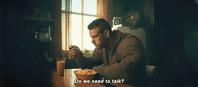 a man with long hair and a beard is sitting in a dark room and talking to someone .