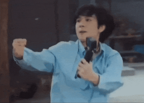 a man in a blue shirt is holding a microphone in his right hand .
