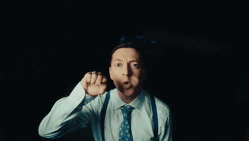 a man wearing suspenders and a tie holds up his fist