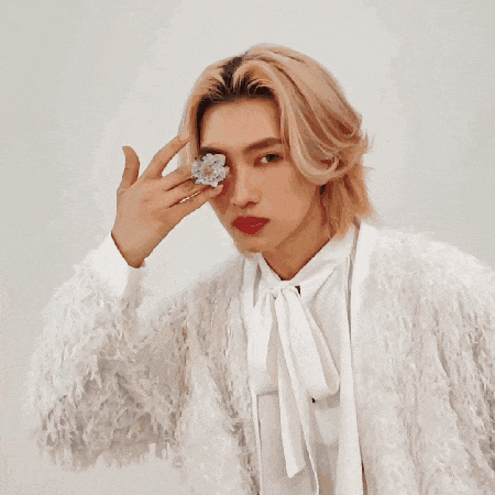 a man with long blonde hair wearing a white fur coat and red lipstick
