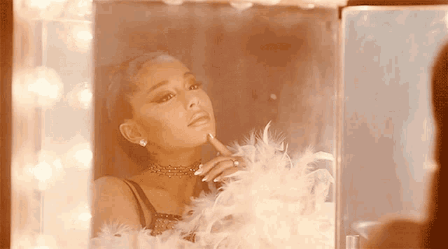 a woman looks at herself in a mirror with feathers around her neck