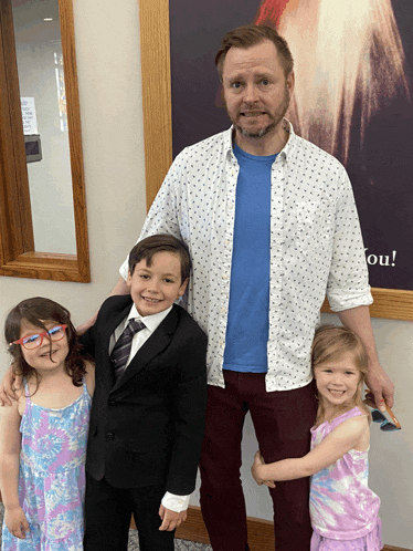 a man and three children pose for a picture in front of a jesus picture