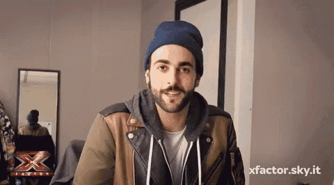 a man with a beard is wearing a beanie and a jacket with the x factor logo on the bottom