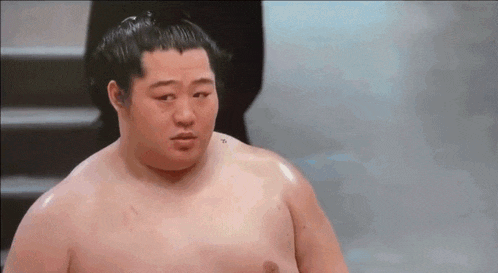 a shirtless sumo wrestler with a tattoo on his shoulder looks at the camera .