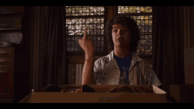 a young boy with curly hair is sitting in a cardboard box and giving the middle finger