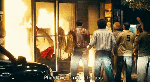 a group of people are standing in front of a building that is on fire and one of them is wearing a number 5 jersey .