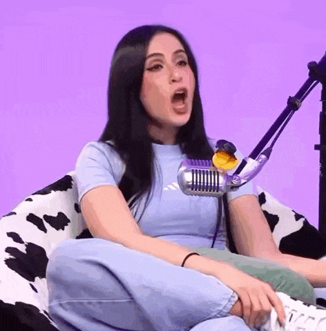 a woman is sitting on a bean bag chair in front of a microphone and making a funny face .