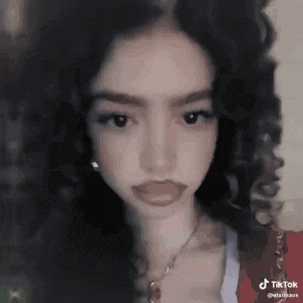 a girl with curly hair and a necklace is looking at the camera .