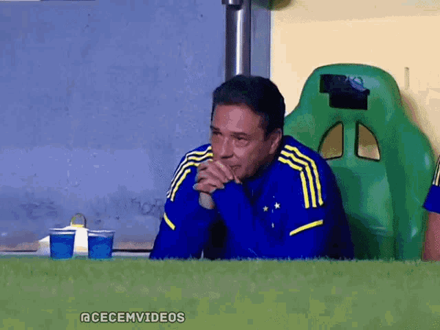 a man wearing a blue and yellow adidas jacket sits in a green seat