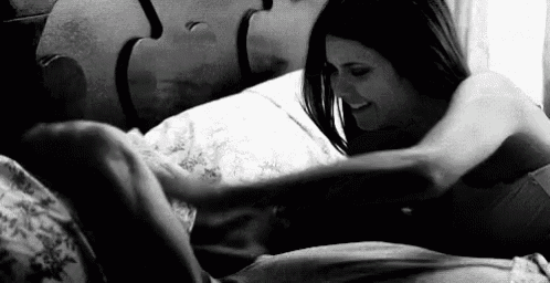 a woman is laying on a bed with a man and touching him .