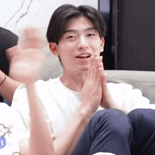 a young man sitting on a couch with his hands folded