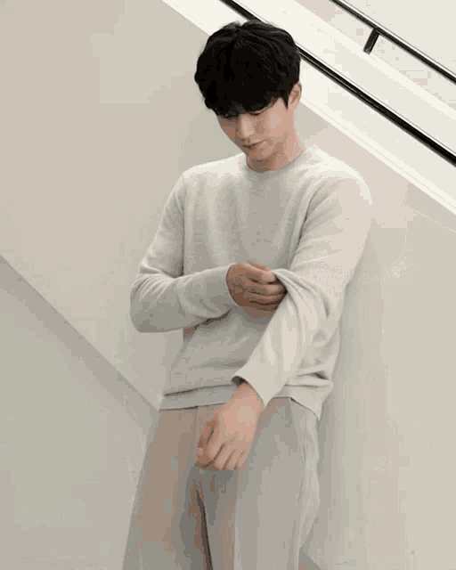 a man wearing a grey sweater and khaki pants is standing in front of stairs