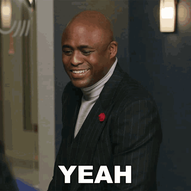 a man in a suit and turtleneck is smiling with the word yeah above him