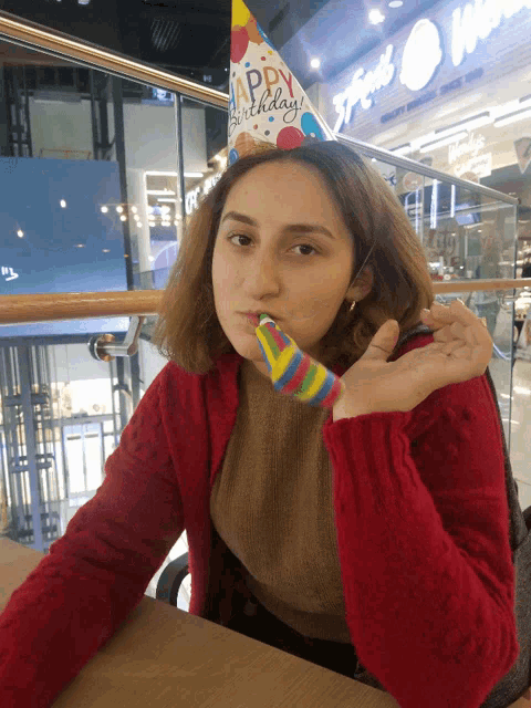 a woman wearing a happy birthday hat holds a party horn in her mouth