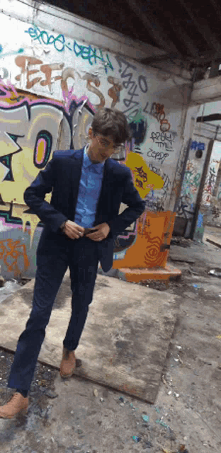a man in a suit is standing in front of a wall with graffiti on it including the word death