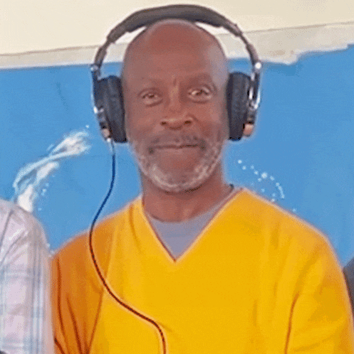 a man wearing headphones and a yellow shirt looks at the camera