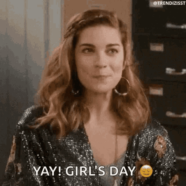 a woman is wearing a sequined jacket and earrings and is saying yay ! girl 's day .
