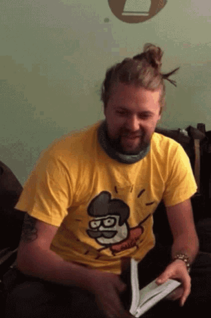 a man wearing a yellow t-shirt with a cartoon character on it is reading a book