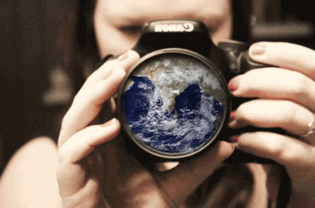 a woman is holding a canon camera with a picture of the earth in the lens