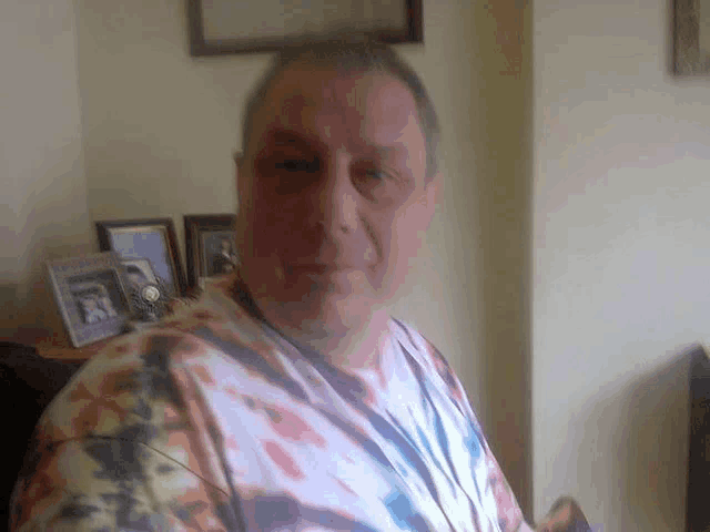 a man wearing a tie dye shirt stands in front of a wall with a few framed pictures on it