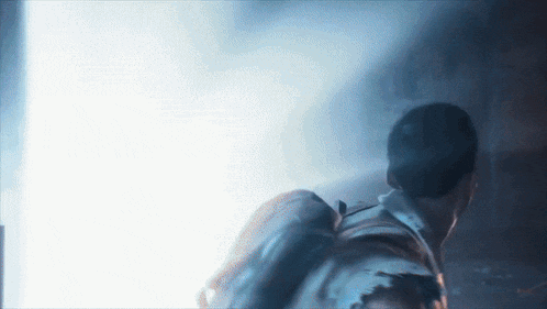 a man with a backpack is walking through a dark room with a light coming through the door