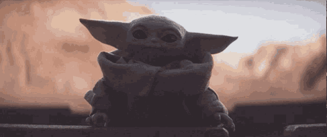 a baby yoda from star wars is sitting on a railing and looking at the camera