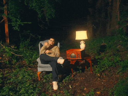 a man sits in a chair next to a record player and lamp