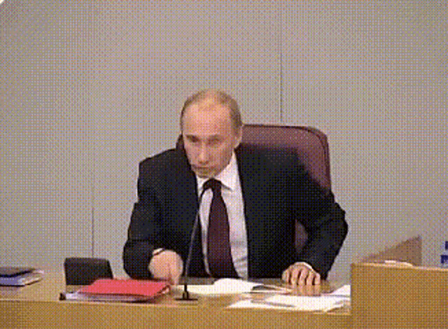 a man in a suit and tie sits at a desk with a microphone