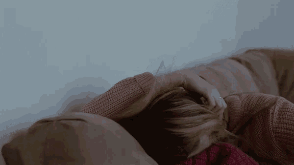 a woman in a pink sweater is laying on a bed with her head on a pillow