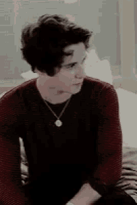 a young man in a red sweater is sitting on a bed .