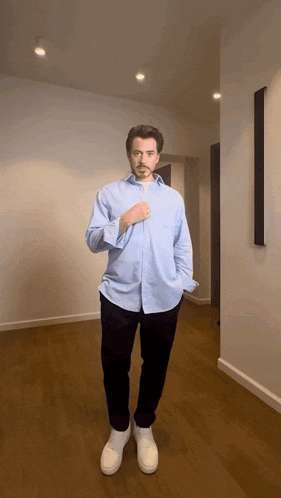 a man wearing a light blue shirt and black pants is standing in a hallway