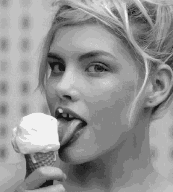 a woman is licking an ice cream cone with her tongue out