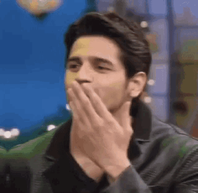 a man is covering his mouth with his hands and looking at the camera .