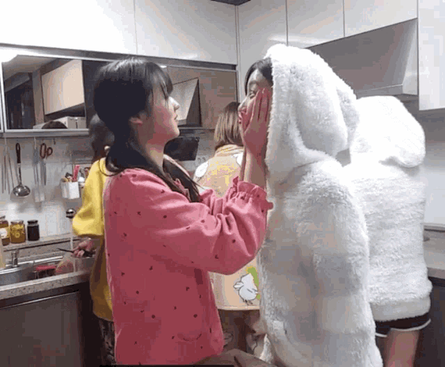 a girl in a pink sweater is touching the face of another girl in a white hoodie